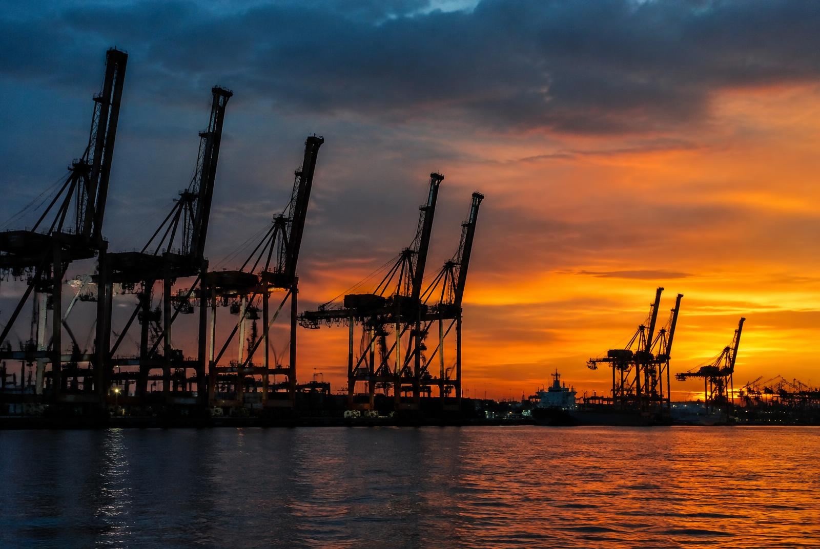 Port gantry cranes silhouetted against an orange sunset